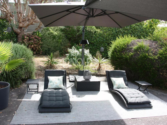 Espace extérieur avec chaises longues et parasol dans un jardin verdoyant.