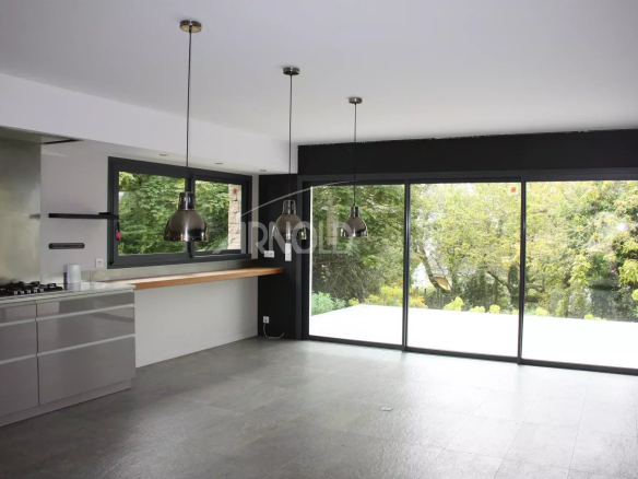 Intérieur d'une maison familiale avec cuisine moderne et grandes fenêtres donnant sur un jardin verdoyant.