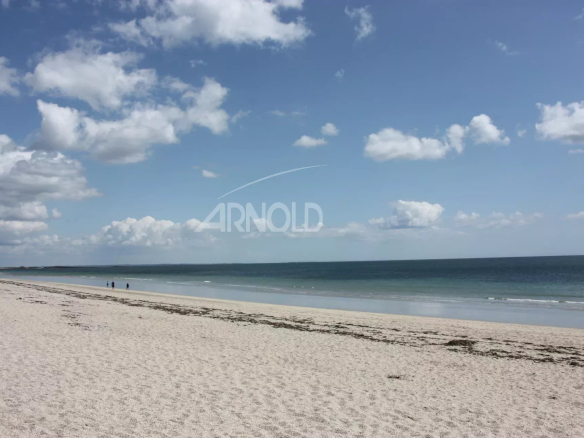 Plage de sable fin avec des personnes au bord de l'eau, ciel bleu et nuages