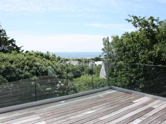 Terrasse en bois avec garde-corps en verre, vue sur la mer et la verdure environnante.