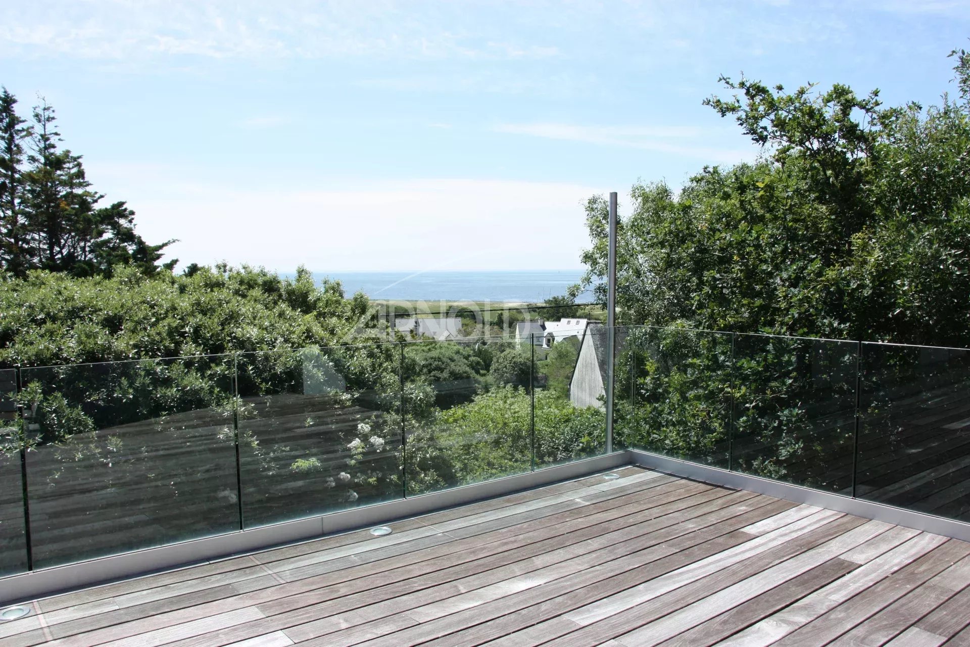 Terrasse avec vue sur la mer Terrasse en bois avec garde-corps en verre, vue sur la mer et la verdure environnante.