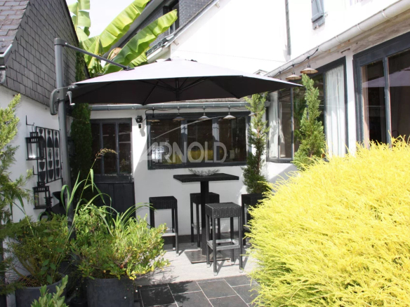 Terrace of a house in Belz with parasol and garden furniture surrounded by greenery.