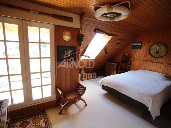 Chambre d'une maison néo-bretonne avec un lit, des poutres apparentes et une fenêtre donnant sur l'extérieur.