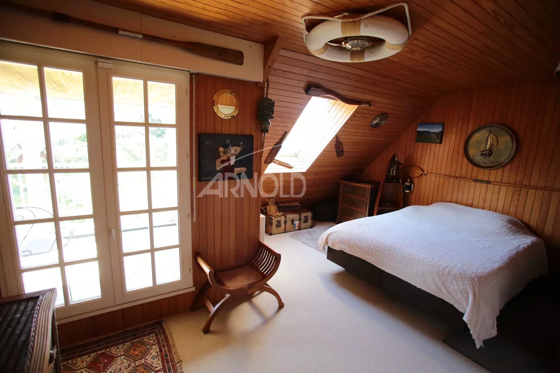Chambre d'une maison néo-bretonne avec un lit, des poutres apparentes et une fenêtre donnant sur l'extérieur.
