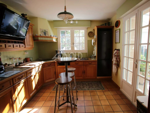Cuisine lumineuse d'une maison néo-bretonne à Vannes avec meubles en bois et grande fenêtre.