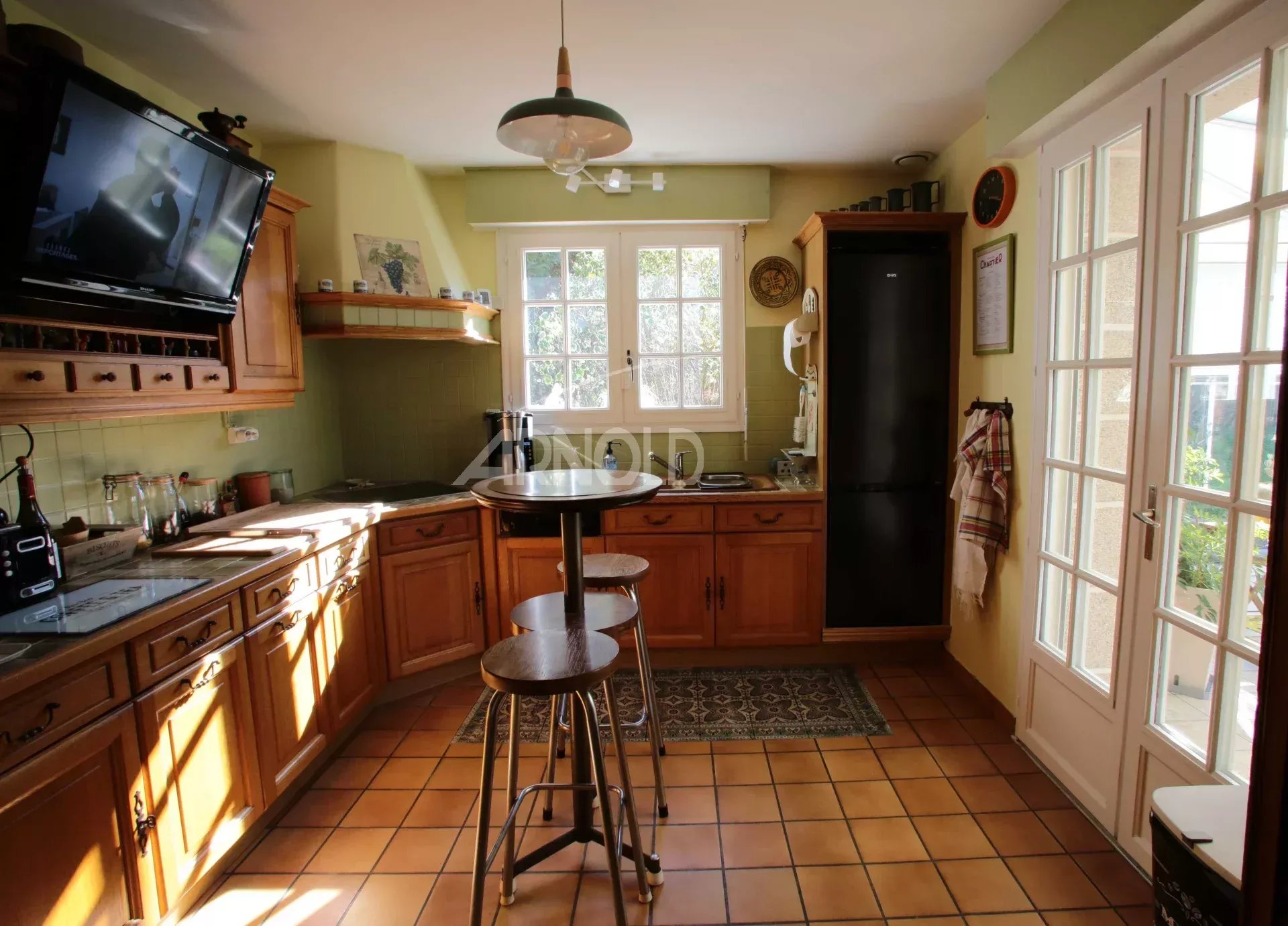 Cuisine lumineuse d'une maison néo-bretonne à Vannes avec meubles en bois et grande fenêtre.