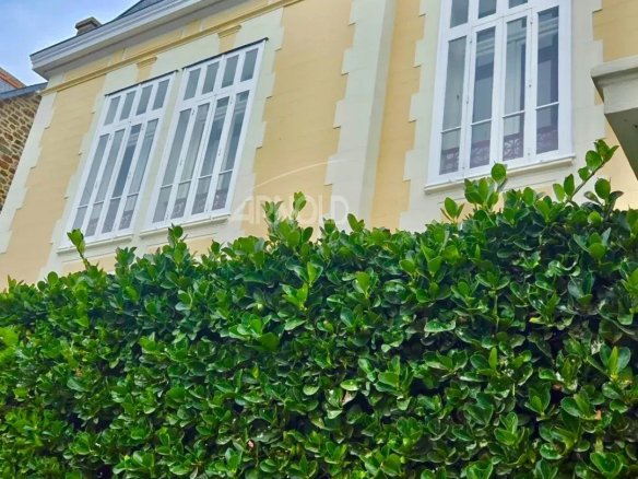 A bourgeois stone house in Saint-Malo, with white windows and a green hedge in front.
