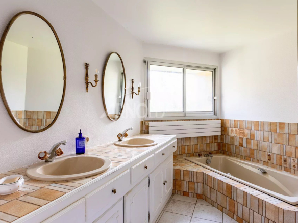 Salle de bain moderne avec deux lavabos, baignoire et fenêtres, décorée de carrelage beige.