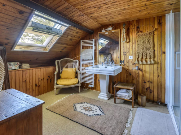 Salle de bain avec poutres en bois, lavabo et fenêtre de toit dans une maison à Saint-Étienne-de-Montluc.