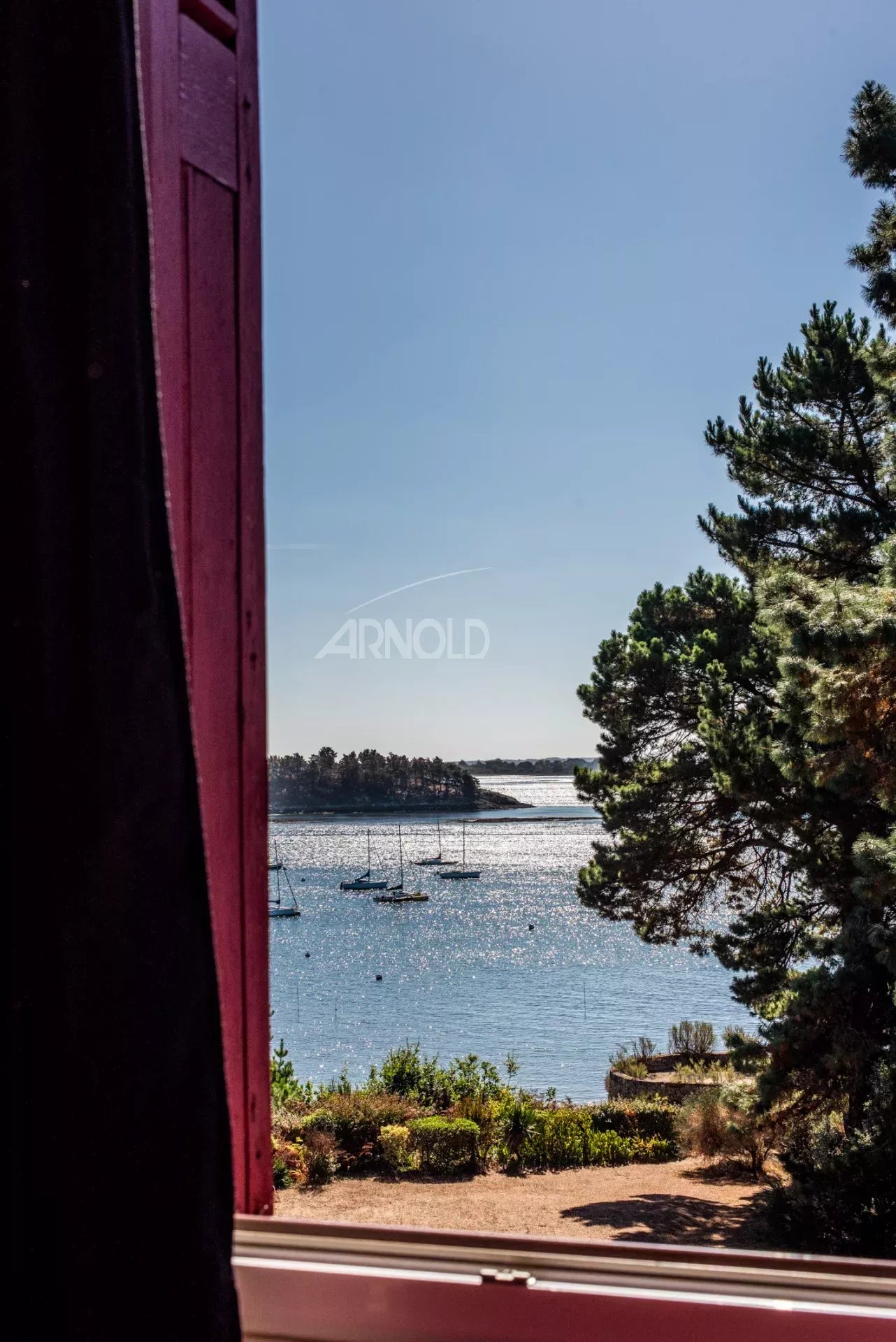 Vue sur le Golfe du Morbihan Vue panoramique sur le Golfe du Morbihan depuis une fenêtre, avec des voiliers et des arbres au premier plan.