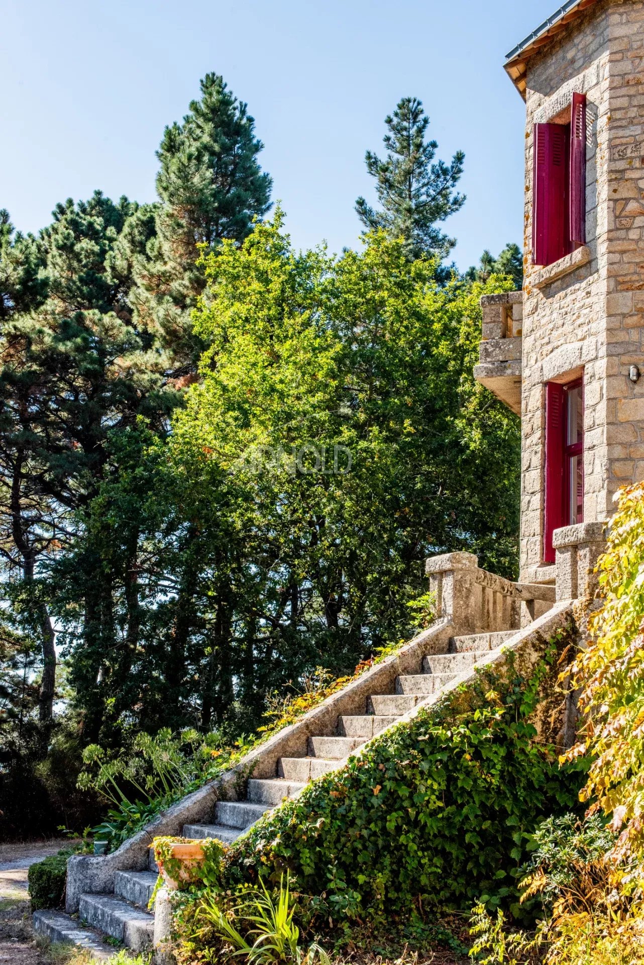 Propriété d’exception à Arradon Escalier en pierre menant à une propriété en pierre avec des fenêtres rouges, entourée d'arbres.