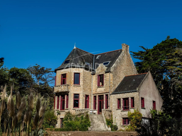 Maison en pierre avec fenêtres rouges, entourée de verdure, située à Arradon, vue sur le Golfe du Morbihan.