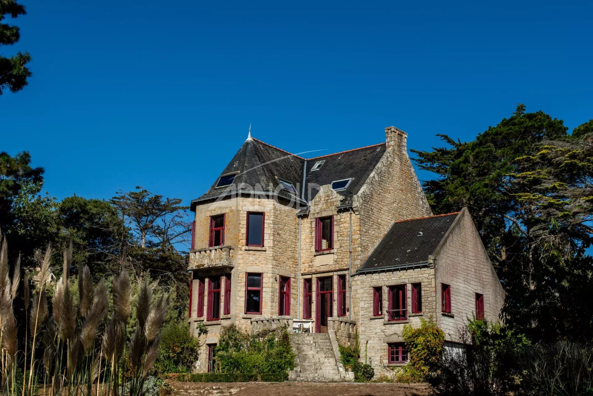 Propriété d’exception à Arradon Maison en pierre avec fenêtres rouges, entourée de verdure, située à Arradon, vue sur le Golfe du Morbihan.