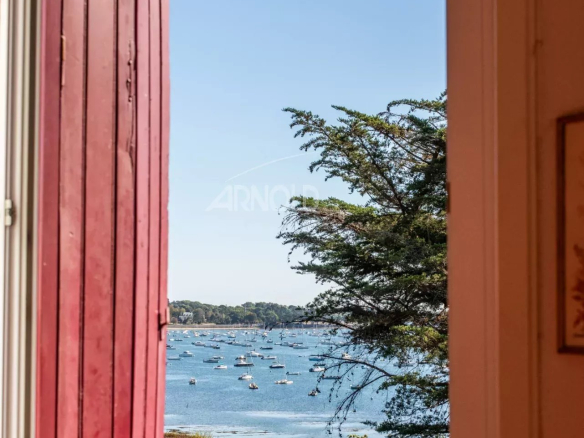 Vue panoramique sur le Golfe du Morbihan depuis une fenêtre avec volets rouges.