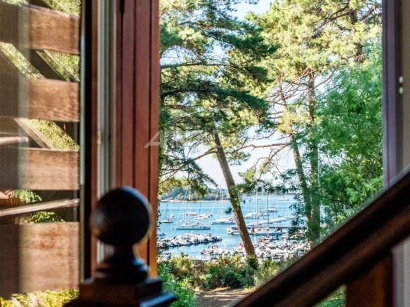 Vue depuis une fenêtre avec des arbres et le Golfe du Morbihan en arrière-plan.