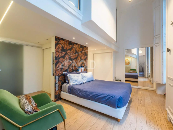 Chambre d'un duplex à Paris 9, avec un grand lit et un mur décoré, éclairée par des fenêtres.