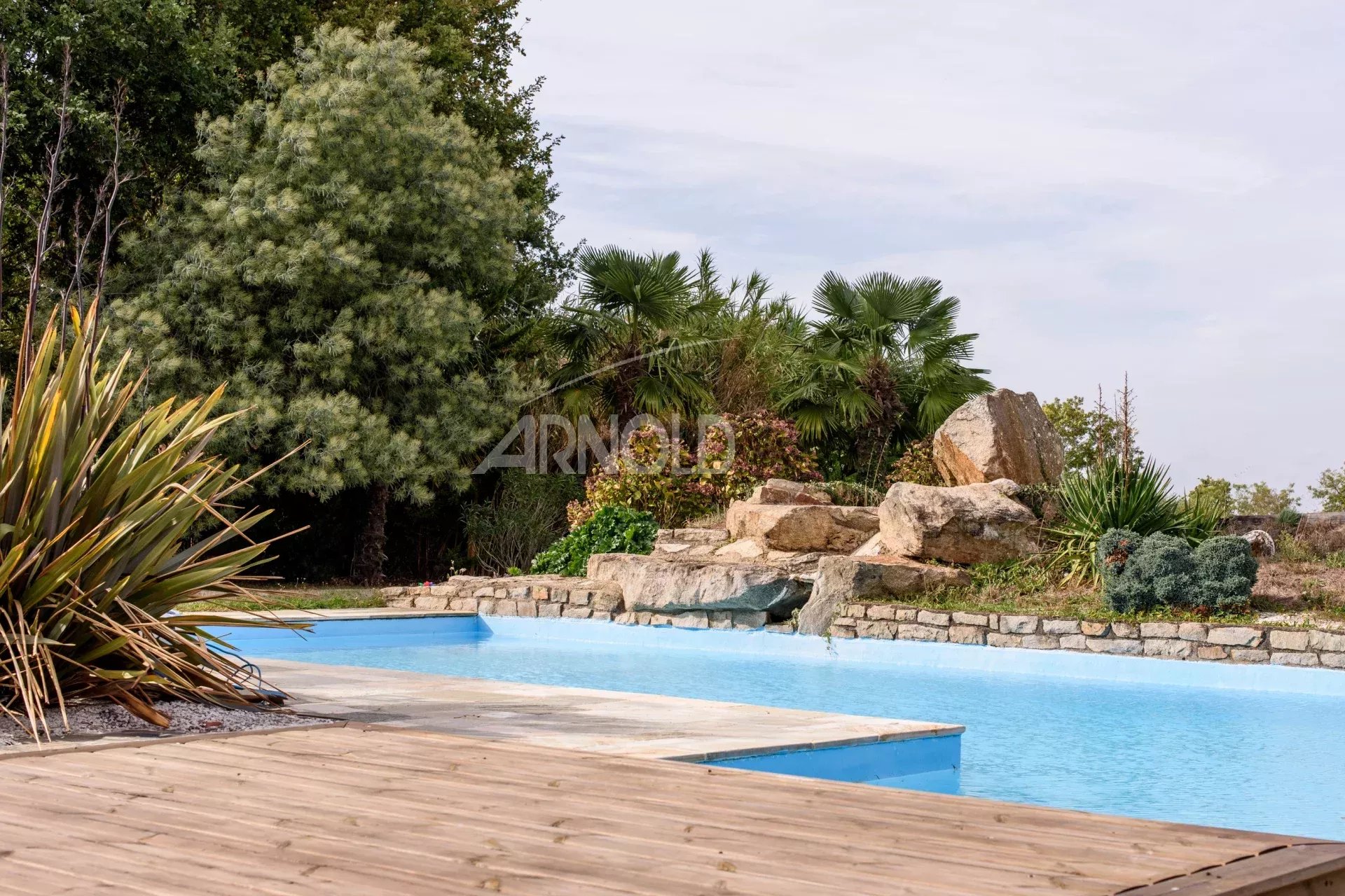 Superb swimming pool in a contemporary farmhouse Swimming pool surrounded by vegetation and rocks in a contemporary property in Surzur.