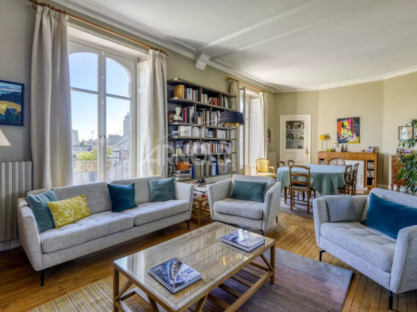Bright living room of a 6-room apartment with sofas and bookcase, windows open to the outside.