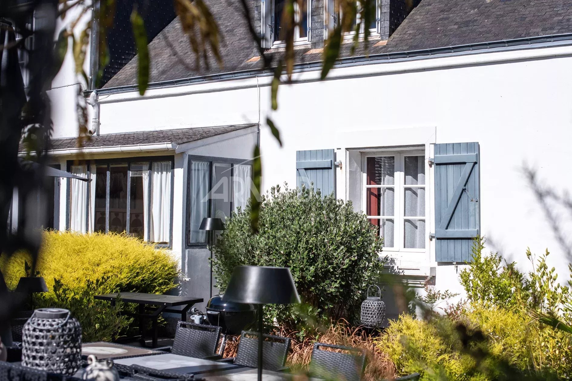 Maison de charme à Belz Maison de charme avec jardin à Belz, fenêtres à volets bleus et mobilier extérieur.