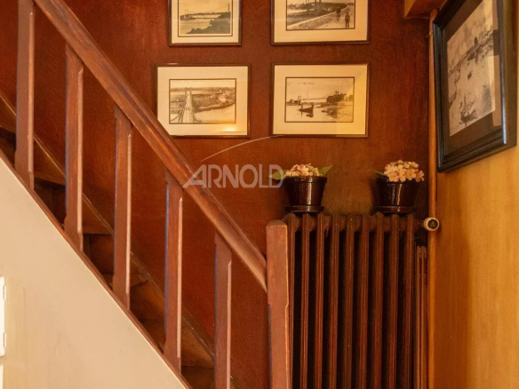 Escalier en bois avec des cadres accrochés au mur et un radiateur en fonte.