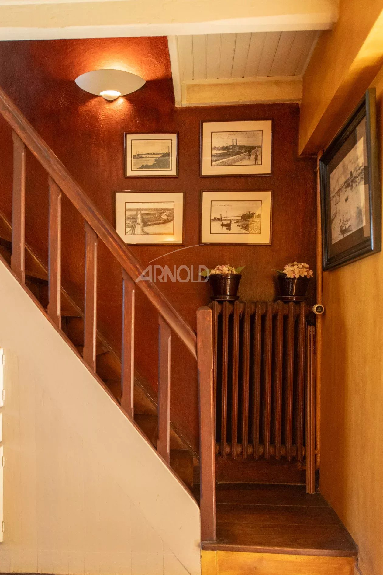 Intérieur d’une maison à Belz Escalier en bois avec des cadres accrochés au mur et un radiateur en fonte.