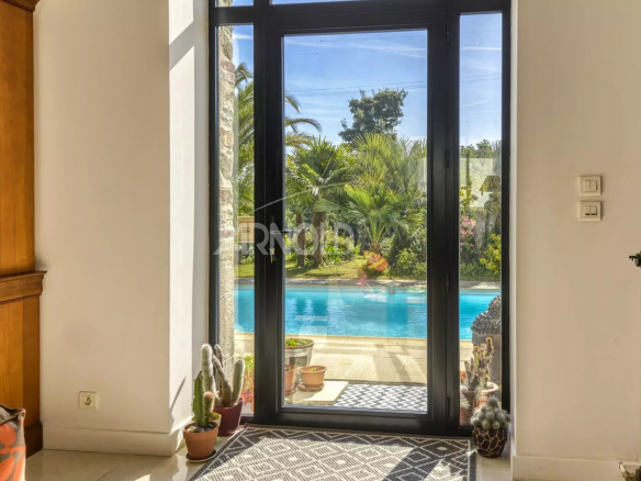 Vue intérieure d'une propriété avec une grande baie vitrée donnant sur une piscine et un jardin paysager.