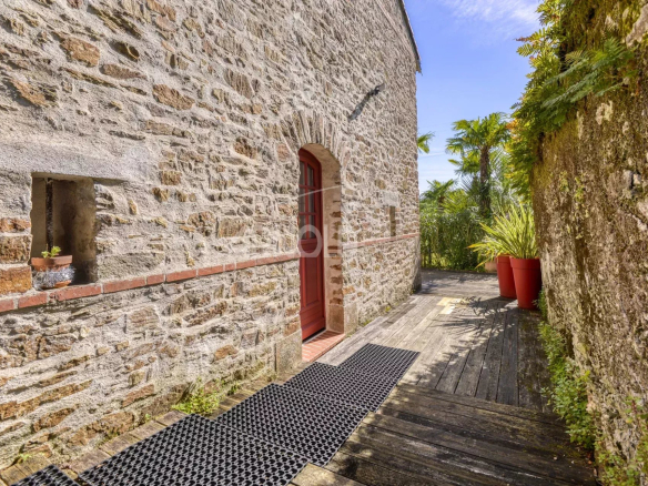 Entrée d'une propriété en pierre avec un chemin en bois et des plantes, Le Pellerin.