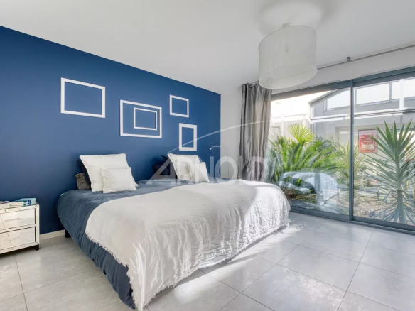 Chambre d'une villa contemporaine avec mur bleu et fenêtres donnant sur un jardin.
