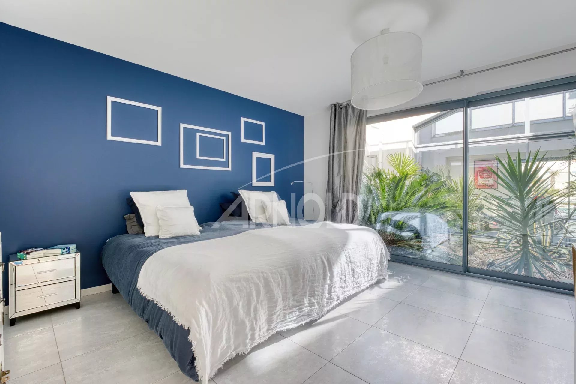 Chambre moderne dans une villa contemporaine Chambre d'une villa contemporaine avec mur bleu et fenêtres donnant sur un jardin.