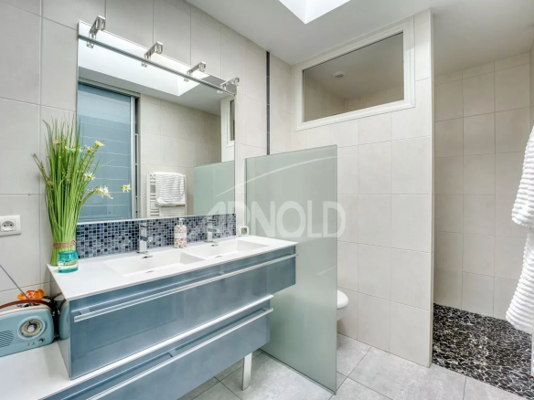 Salle de bains moderne avec double vasque et douche, décorée de carrelage clair.