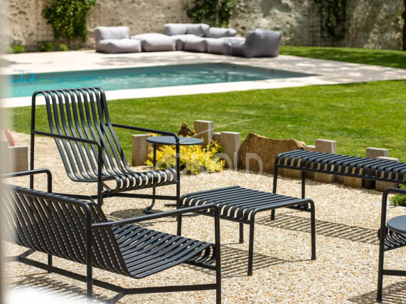 Terrace with chairs and table, swimming pool in the background, green garden