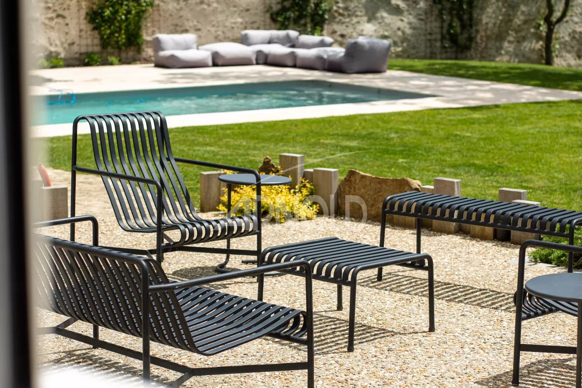 Terrace with chairs and table, swimming pool in the background, green garden