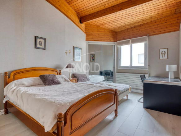 Spacious room with double bed, desk and window, decorated with a wooden ceiling.