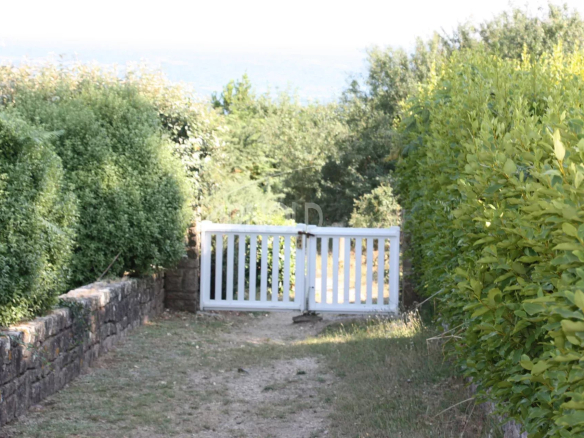 Accès à un chemin menant à la plage, entouré de haies et d'une clôture blanche.