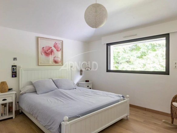 Chambre d'une maison contemporaine avec lit double et fenêtre donnant sur un espace verdoyant.