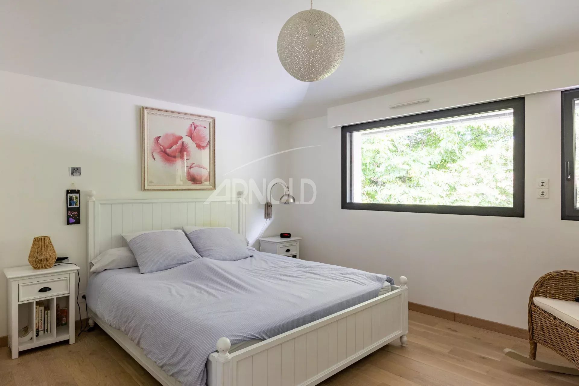 Chambre d'une maison contemporaine avec lit double et fenêtre donnant sur un espace verdoyant.