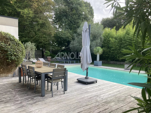 Terrasse en bois avec table et chaises près d'une piscine chauffée dans un jardin verdoyant.
