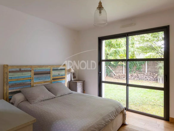 Chambre d'une maison contemporaine avec lit et grande fenêtre donnant sur un jardin.