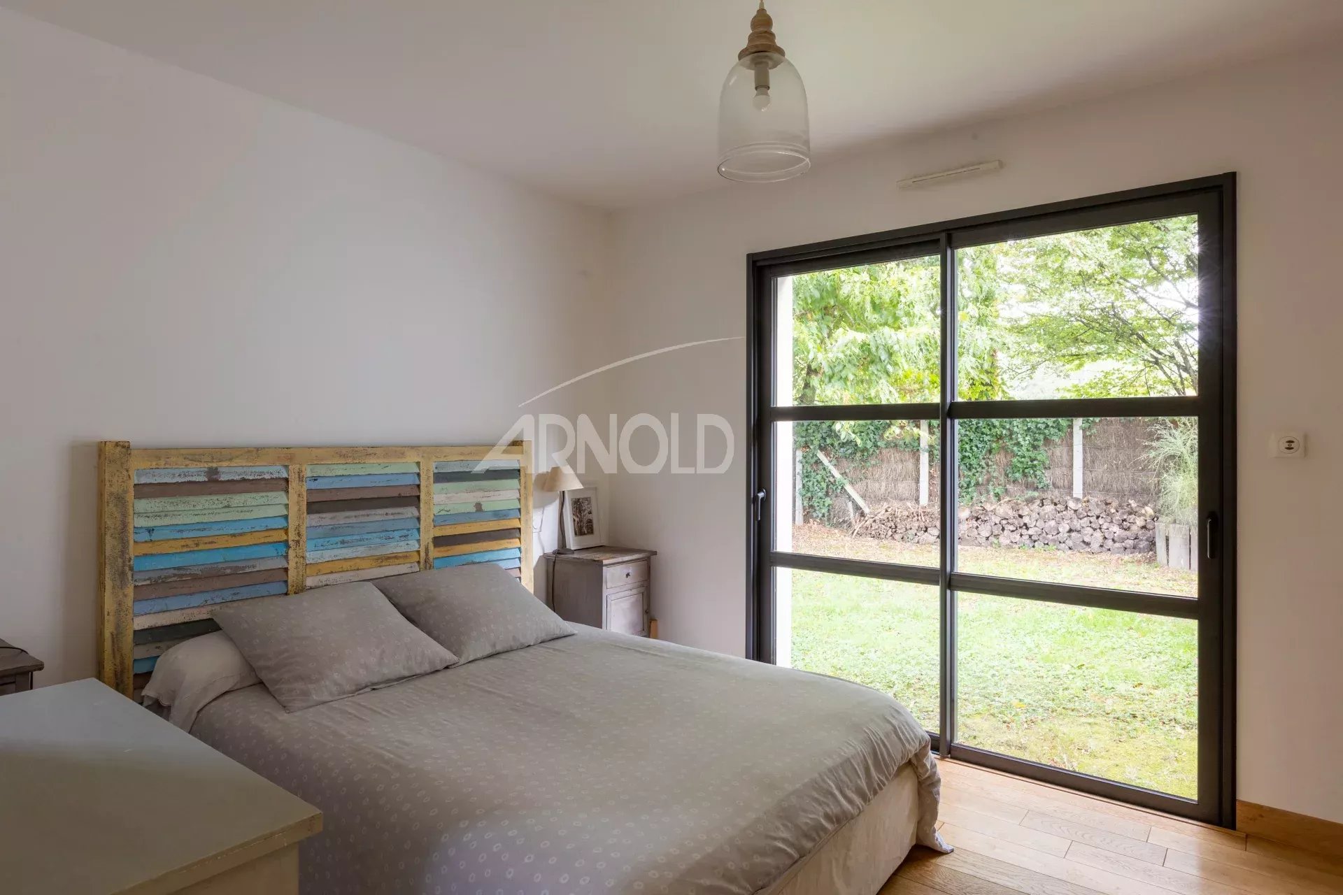 Chambre d'une maison contemporaine avec lit et grande fenêtre donnant sur un jardin.