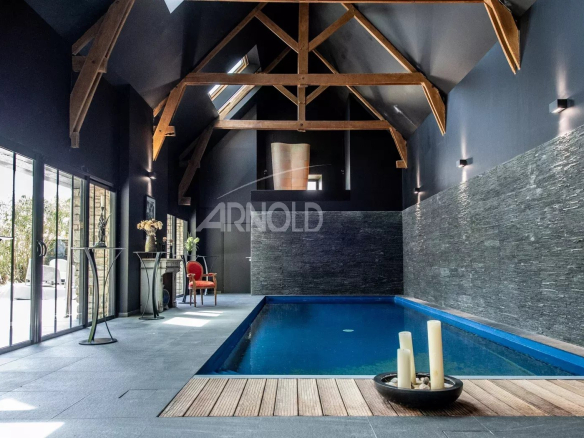 Intérieur d'une propriété avec piscine, poutres apparentes et murs en pierre, éclairage moderne.