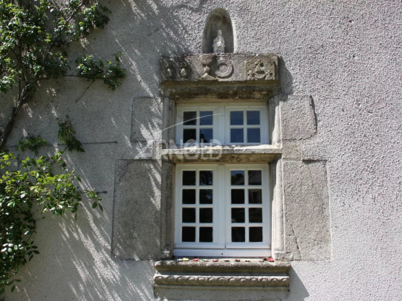 Fenêtre en pierre avec encadrement décoratif sur une façade en plâtre.