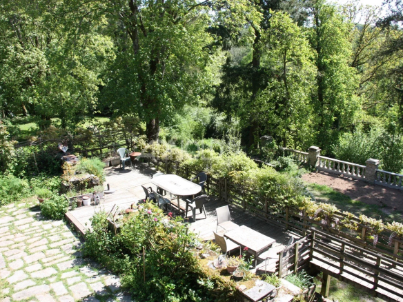 Vue d'un jardin verdoyant avec terrasse en bois et mobilier, entouré d'arbres.