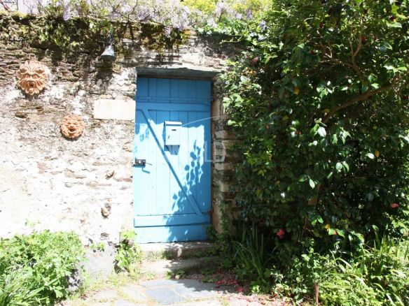 Porte bleue en bois encadrée par des plantes et un mur en pierre.