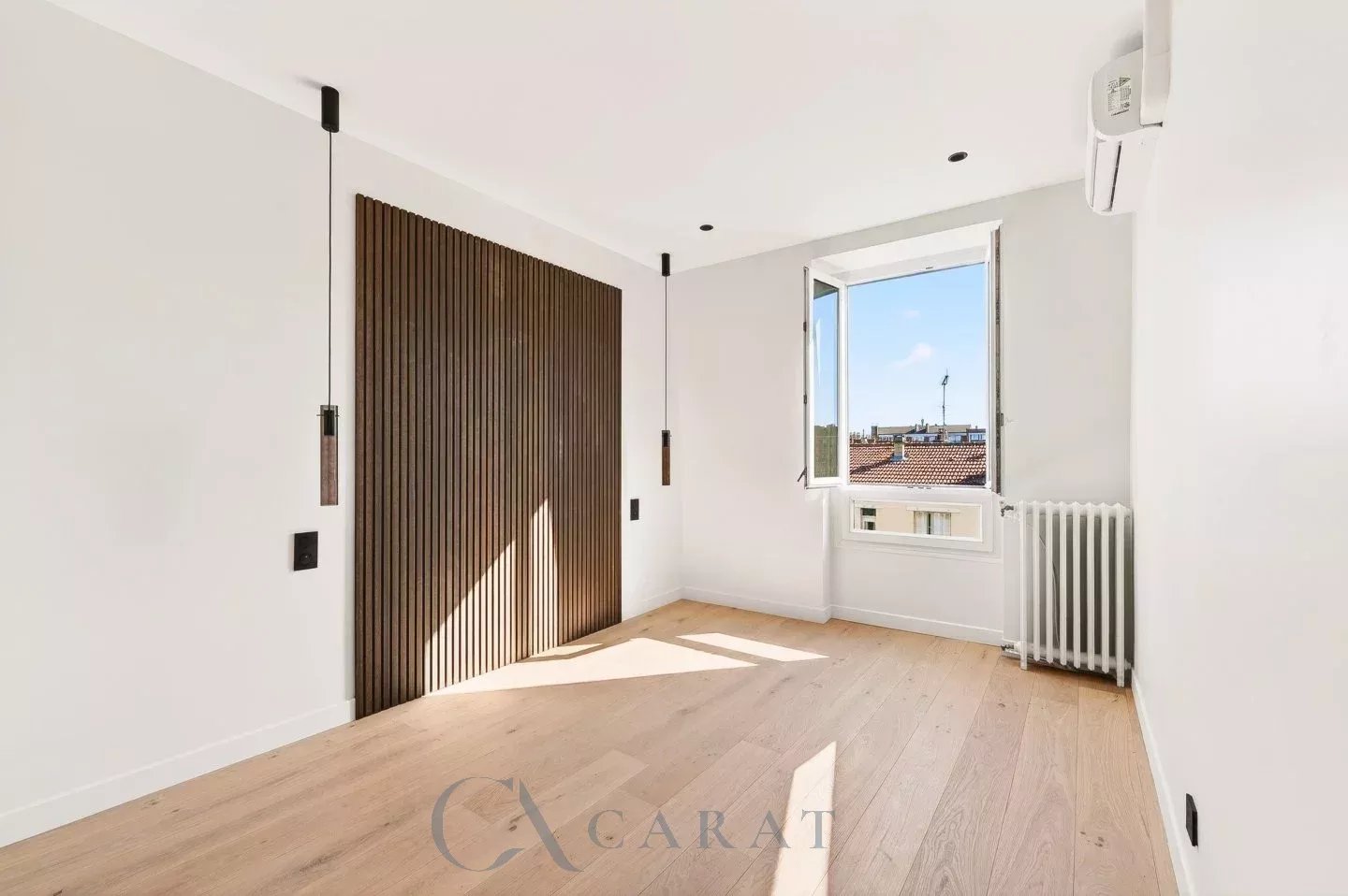 2444d59bfaca25de299f847c432780ad_a33ea8e456_1440-original Bright, modern empty room with a dark wooden slat wall, two pendant lights, and a large open window letting in sunlight.