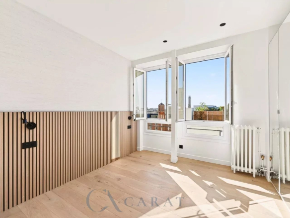 Bright, empty room with large open windows and a city skyline view, light wood floor, and white walls.