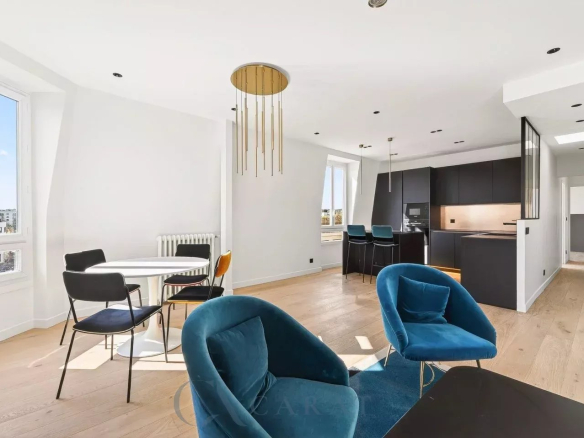 Open-plan living space with blue velvet chairs, a white round dining table, and a dark contemporary kitchen with gold pendant lights.