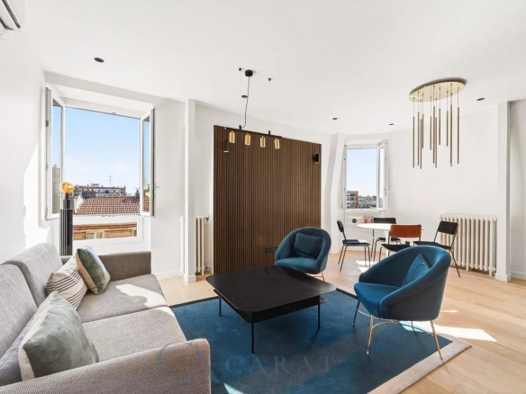 Bright living room with a gray sofa, blue accent chairs, and a wooden slat divider, under sunny windows on the left and right side.