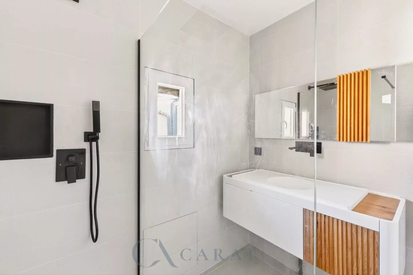9a6a8b86e6948d8d53a8ad69c86c4618_0a4240f8c8_1440-original Modern grey-tiled bathroom with a glass shower partition, black fixtures, and a white vanity with wood accents.