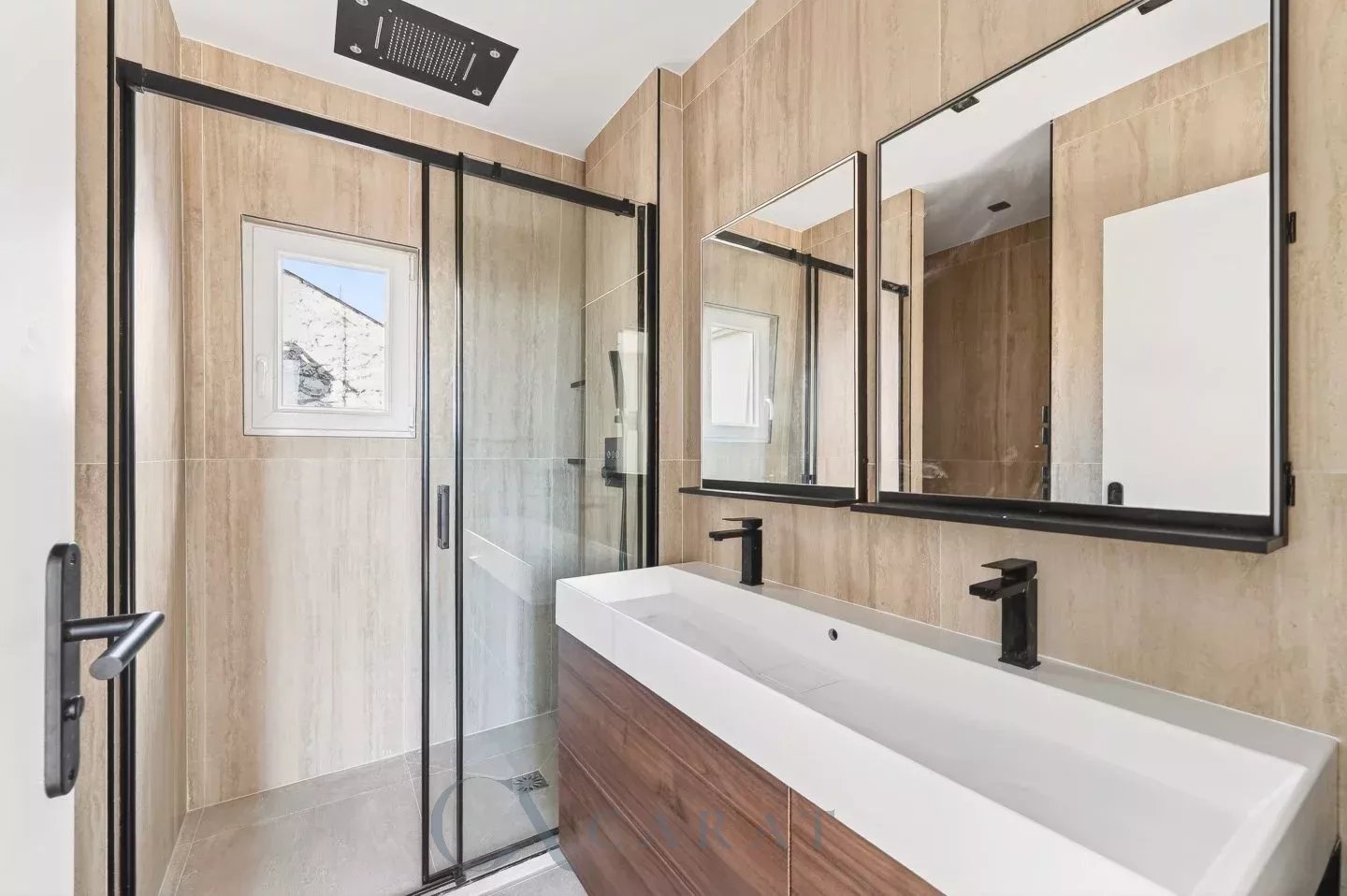 f1646a1b19c950945efe877af50357ff_127546a851_1440-original Modern bathroom with tan tile walls, a double white sink vanity with black fixtures, large mirrors, and a glass shower enclosure.