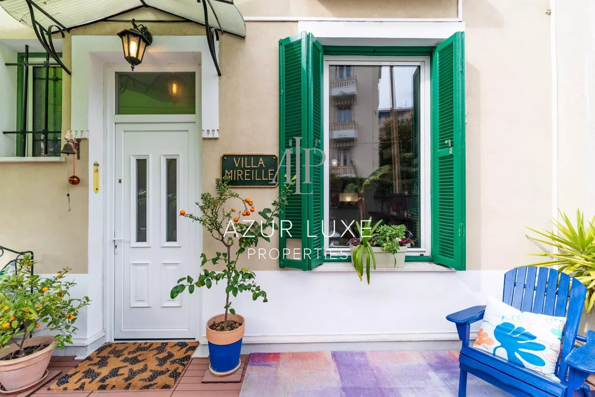 Entrance to Villa Mireille in Nice Entrance to Villa Mireille in Nice with white door and green shutters, potted plants and garden furniture.